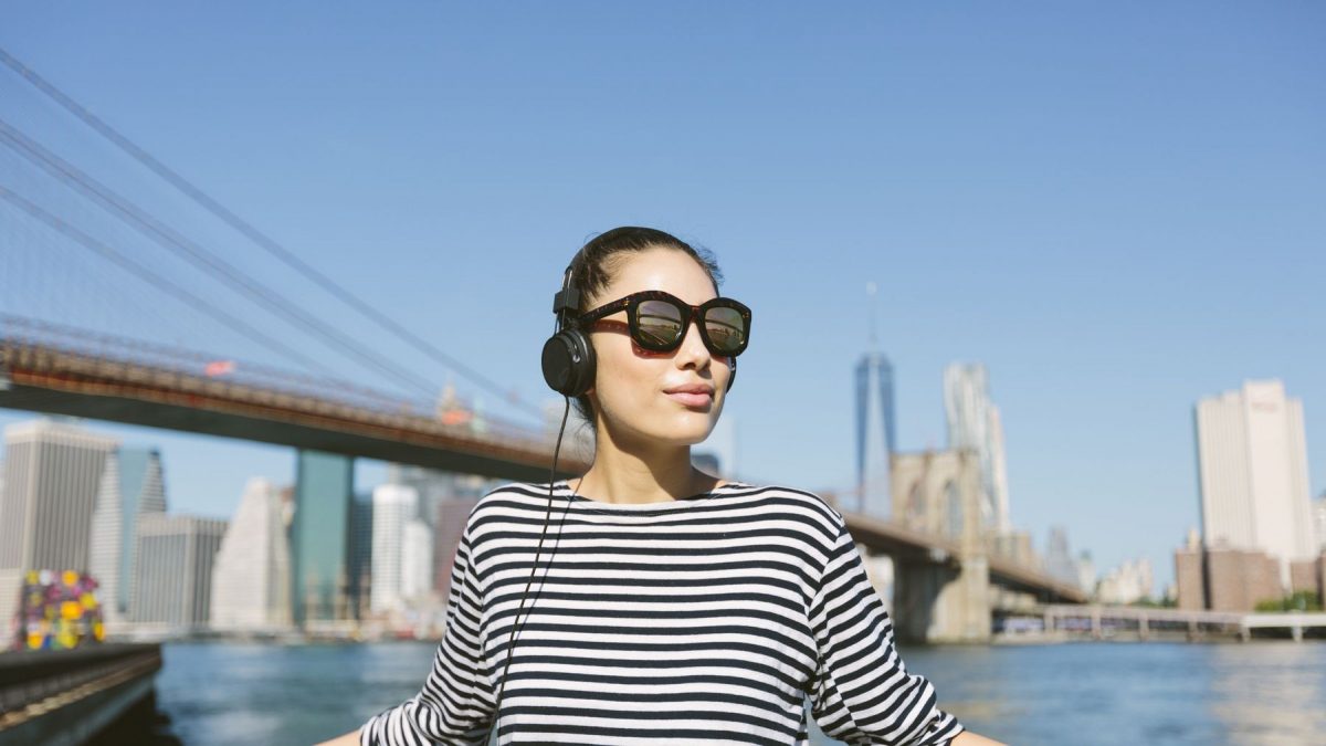 Một cô gái đang đeo tai nghe vừa cập nhật tin tức vừa đứng thư giãn trên cầu